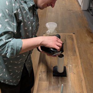 Pouring beans into a Coffee grinder. A Brewing space full of coffee equipment like the Fellow Stagg Pour over kettle and hario v60. The Scale Is a Timemore Blackmirror Nano and the Grinder a Timemore Chestnut c3.